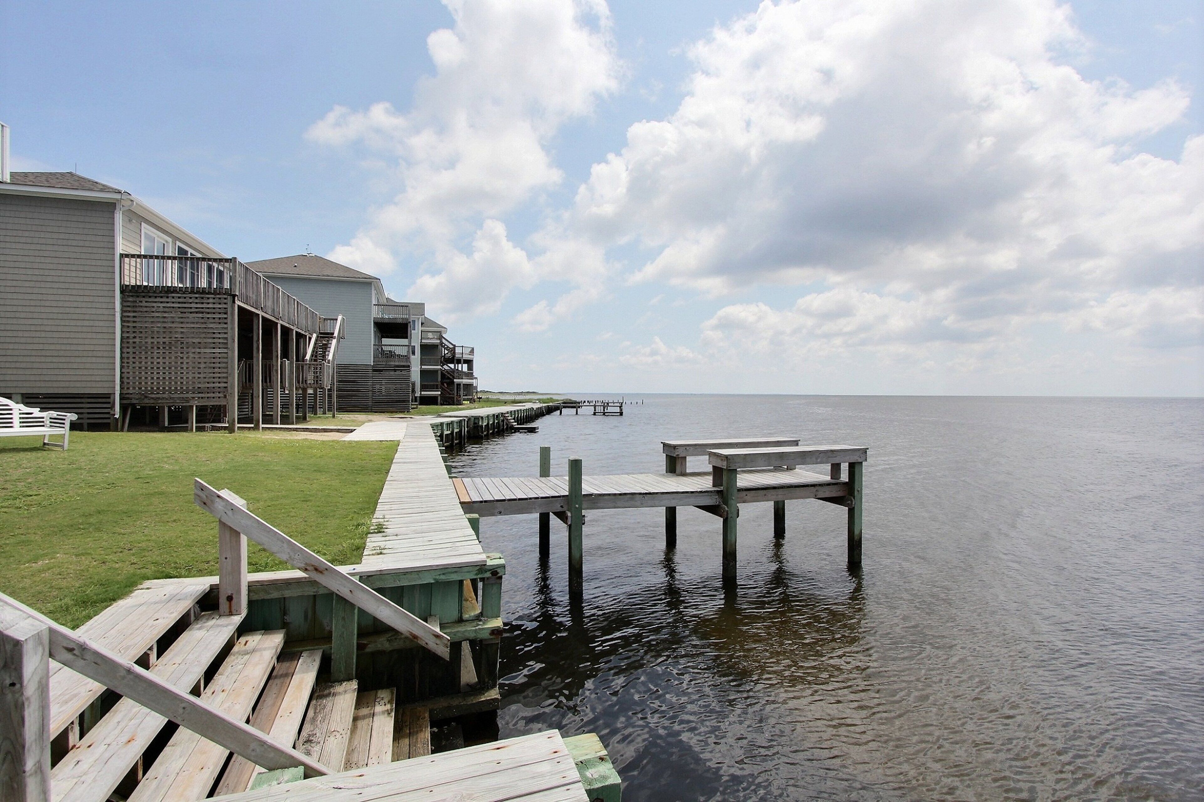 A waterfront property with a wooden dock extending into the water, a grassy area, and a building with multiple balconies.