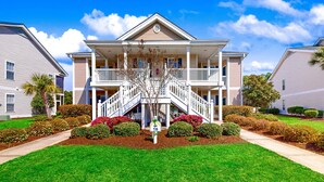 A two-story building with a central staircase, surrounded by well-maintained gardens and a clear sky. - Sunset Village 16-D: Top Floor, Pool, Hot Tub (Sunset Beach)