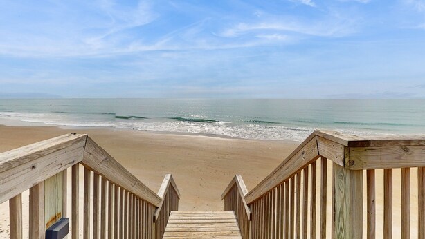Una scala di legno conduce a una spiaggia sotto un cielo sereno.