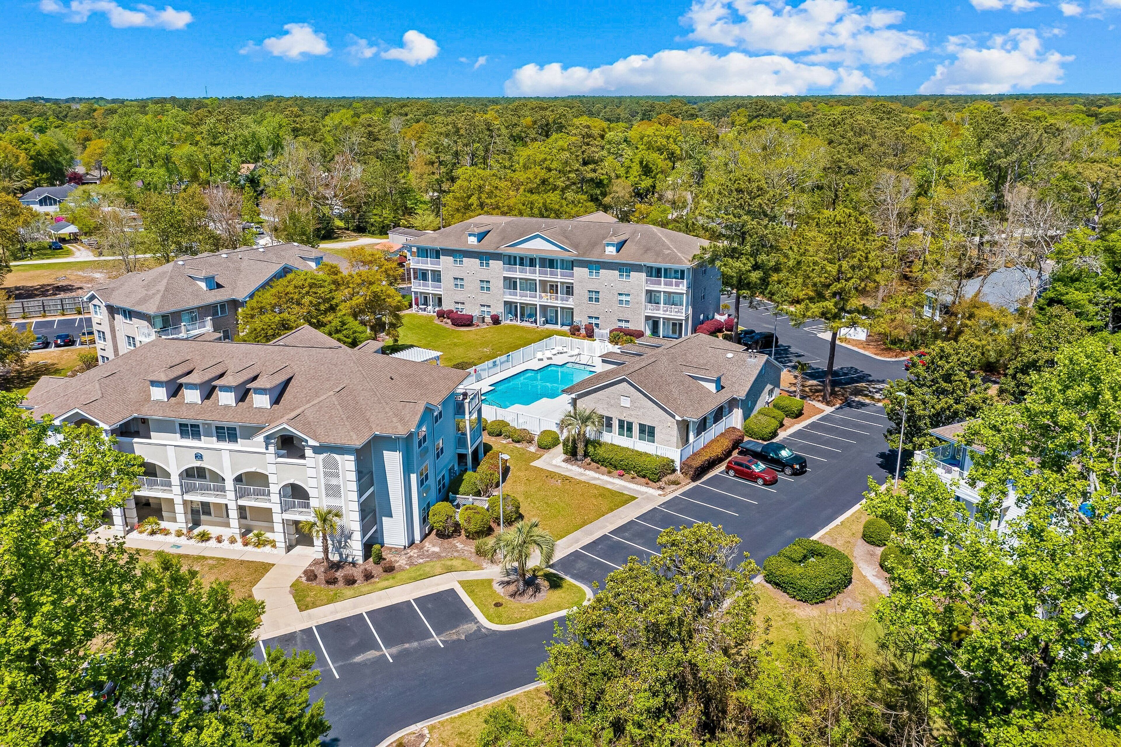 A multi-story hotel with a swimming pool, parking lot, and surrounding greenery.