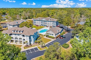 A multi-story hotel with a swimming pool, parking lot, and surrounding greenery.