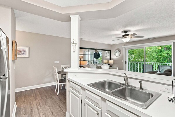 A kitchen with a central island, double sinks, and a dining area with a chair.