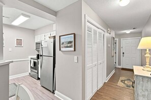 A modern kitchen with stainless steel appliances, a dining area with a table and chairs, and a hallway with a door and a lamp. - Blue Heron Hideaway | Sleeps 6 | Pools & Hot Tub (Sunset Beach)