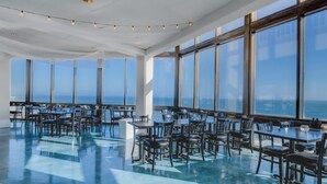 A spacious dining area with large windows offering ocean views, tables and chairs arranged for dining, and a polished floor. - Oceanfront retreat with pool, sauna, beach access, and golf nearby (North Topsail Beach)