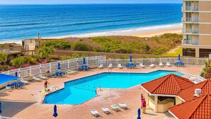 A pool area with a view of the ocean, lounge chairs, and a building with balconies. - Oceanfront retreat with pool, sauna, beach access, and golf nearby (North Topsail Beach)