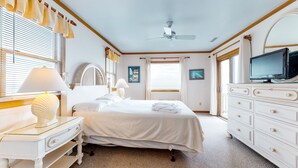Une chambre d’hôtel comprenant un lit, une télévision, une commode, un bureau avec une lampe et une fenêtre avec des rideaux.