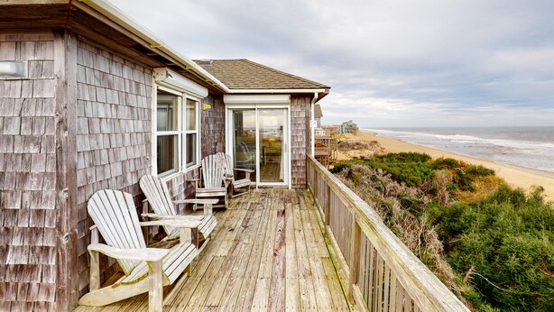 Une terrasse en bois avec des fauteuils Adirondack donnant sur une plage.