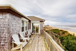 Une terrasse en bois avec des fauteuils Adirondack donnant sur une plage.