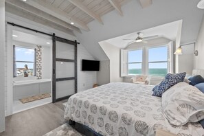 Quarto com cama grande, TV fixada na parede e vista para o oceano pela janela.
