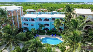 Un resort con una piscina centrale circondata da palme e un edificio a più piani con finestre ad arco.