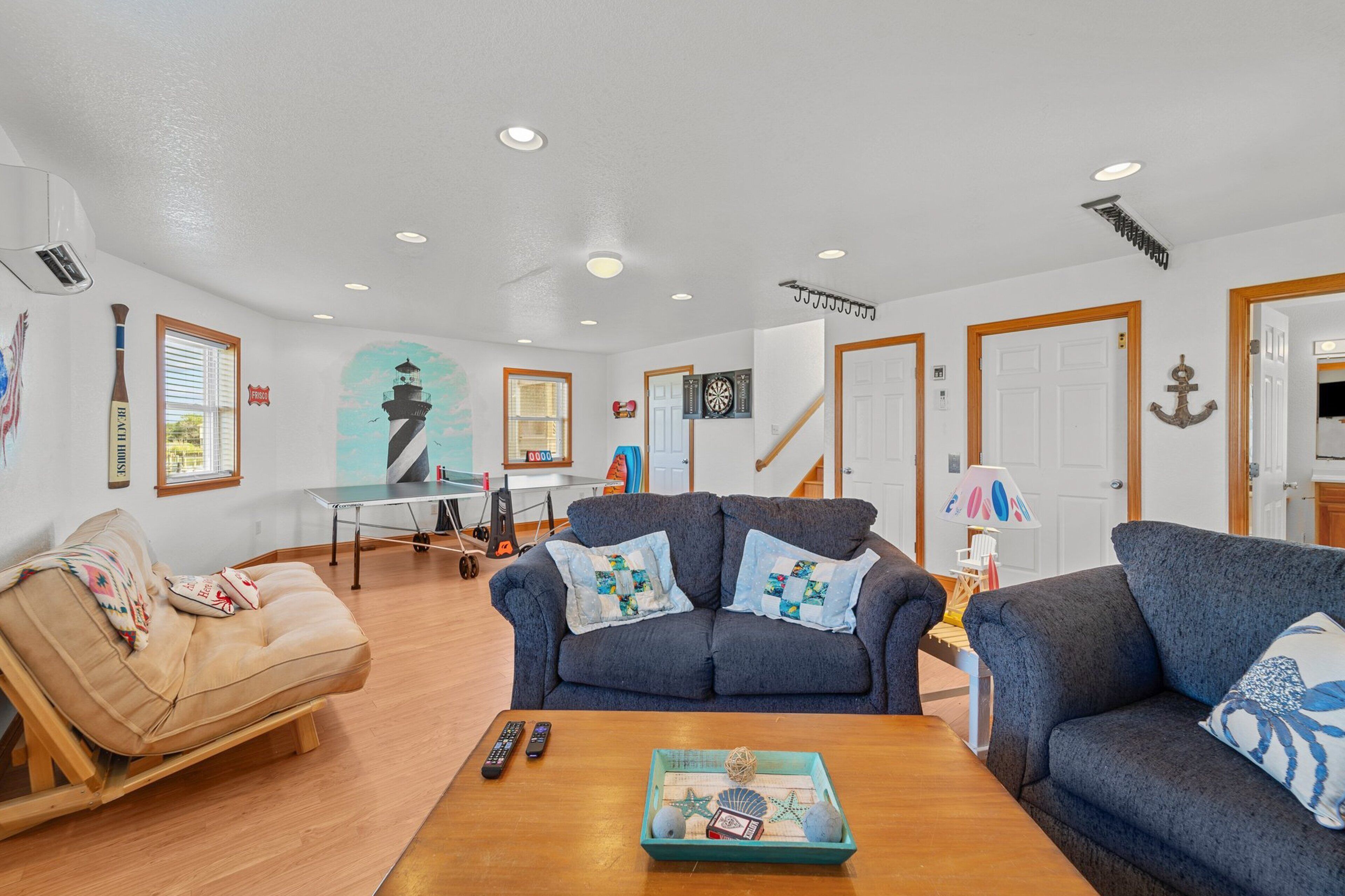 A living room with a sofa, a coffee table with decorative items, a ping pong table, and a mural of a lighthouse.