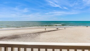 Ein Strand mit blauem Himmel, ruhiger See und einem Holzdeck im Vordergrund.