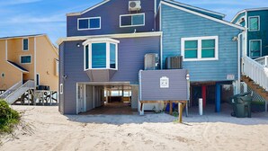 Ein zweistöckiges Strandhaus mit überdachter Veranda, einem Balkon und einem sichtbaren Mülleimer.