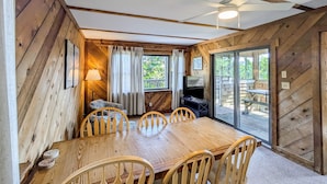 A wooden-paneled room with a large dining table, chairs, a TV, and a sliding glass door to an outdoor deck. - Classic, Dog-Friendly Home w/ AC, Shared Pool, High-Speed WiFi - Steps to Beach (Avon)