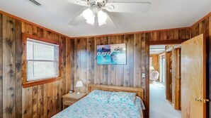 A bedroom with wooden paneling, a bed with floral bedding, a ceiling fan, a window with blinds, and a door leading to another room. - Classic, Dog-Friendly Home w/ AC, Shared Pool, High-Speed WiFi - Steps to Beach (Avon)