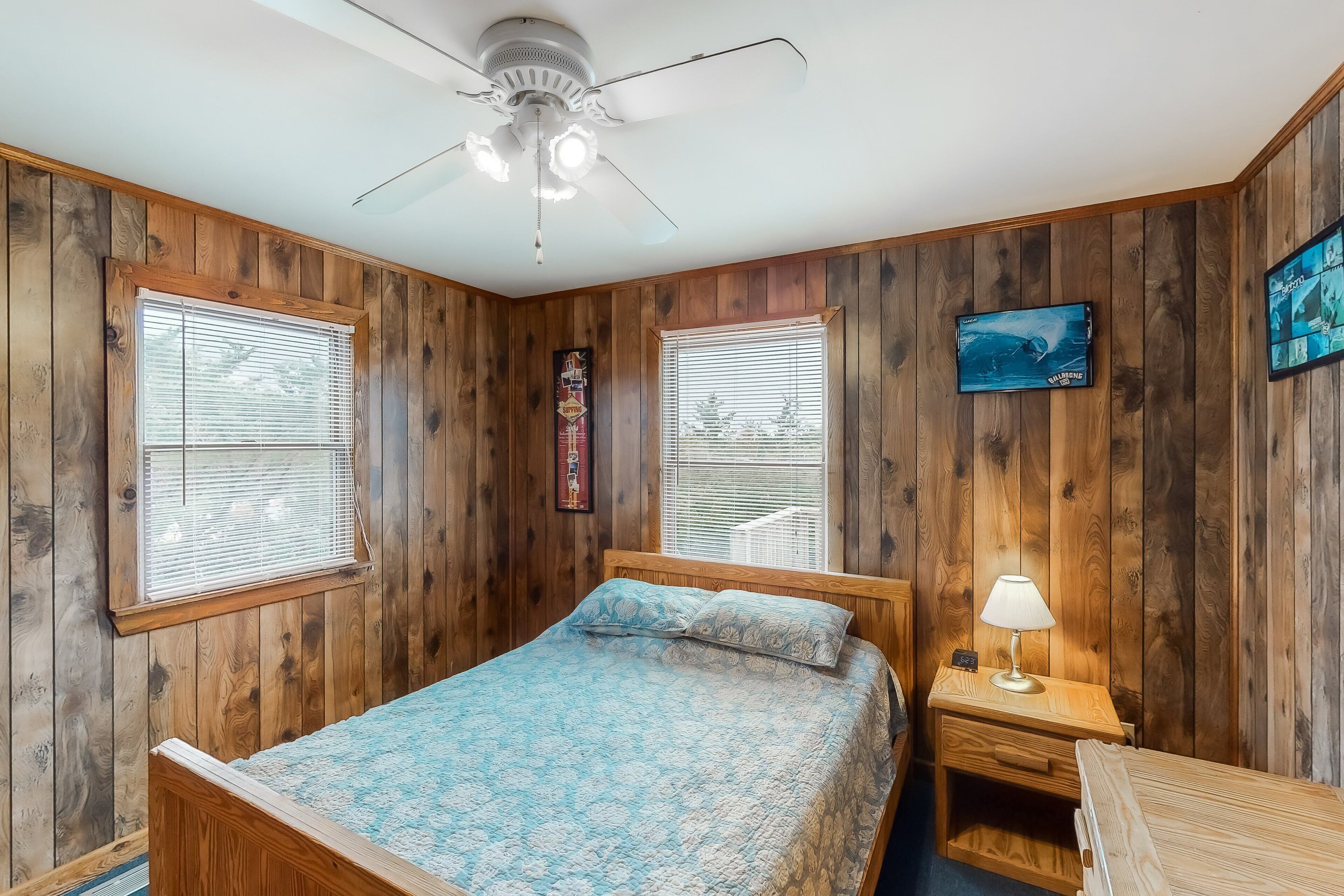 Una habitación con paneles de madera, una cama, una mesita de noche, una lámpara y un ventilador de techo.