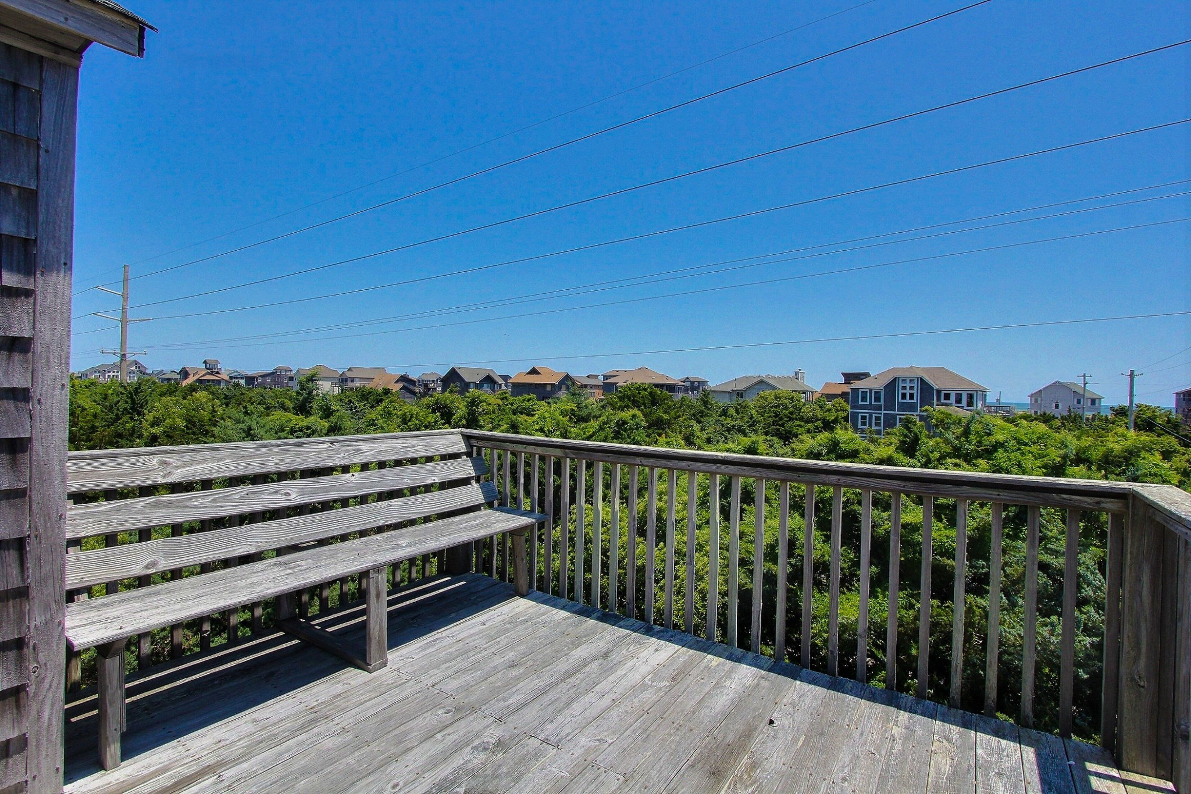 A wooden deck with a railing overlooking a residential area with houses and greenery.