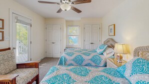 A bedroom with a ceiling fan, a bed with patterned bedding, a nightstand with a lamp, and a view of a balcony through a window. - Waterfront home with private pool, hot tub, pool table & fireplace -dog-friendly (Avon)