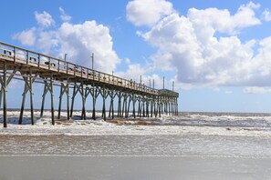 A pier extending into the ocean with a clear sky and waves crashing against it. - Back 9 and Beach Time: Fairway View Condo (Sunset Beach)