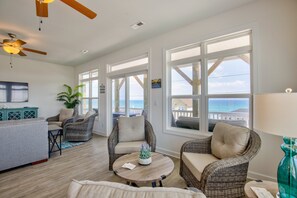 A spacious living room with large windows, wicker furniture, a ceiling fan, and a view of the ocean.
