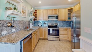 A kitchen with granite countertops, stainless steel appliances, wooden cabinets, and white shelving units. - Vibrant beach retreat with washer/dryer, central AC, deck, & pool access (Hatteras)