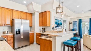 A modern kitchen with wooden cabinets, a stainless steel refrigerator, a dishwasher, and a bar area with stools.