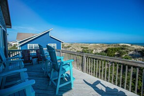 Terraza de madera con sillas Adirondack azules y vista a la playa.