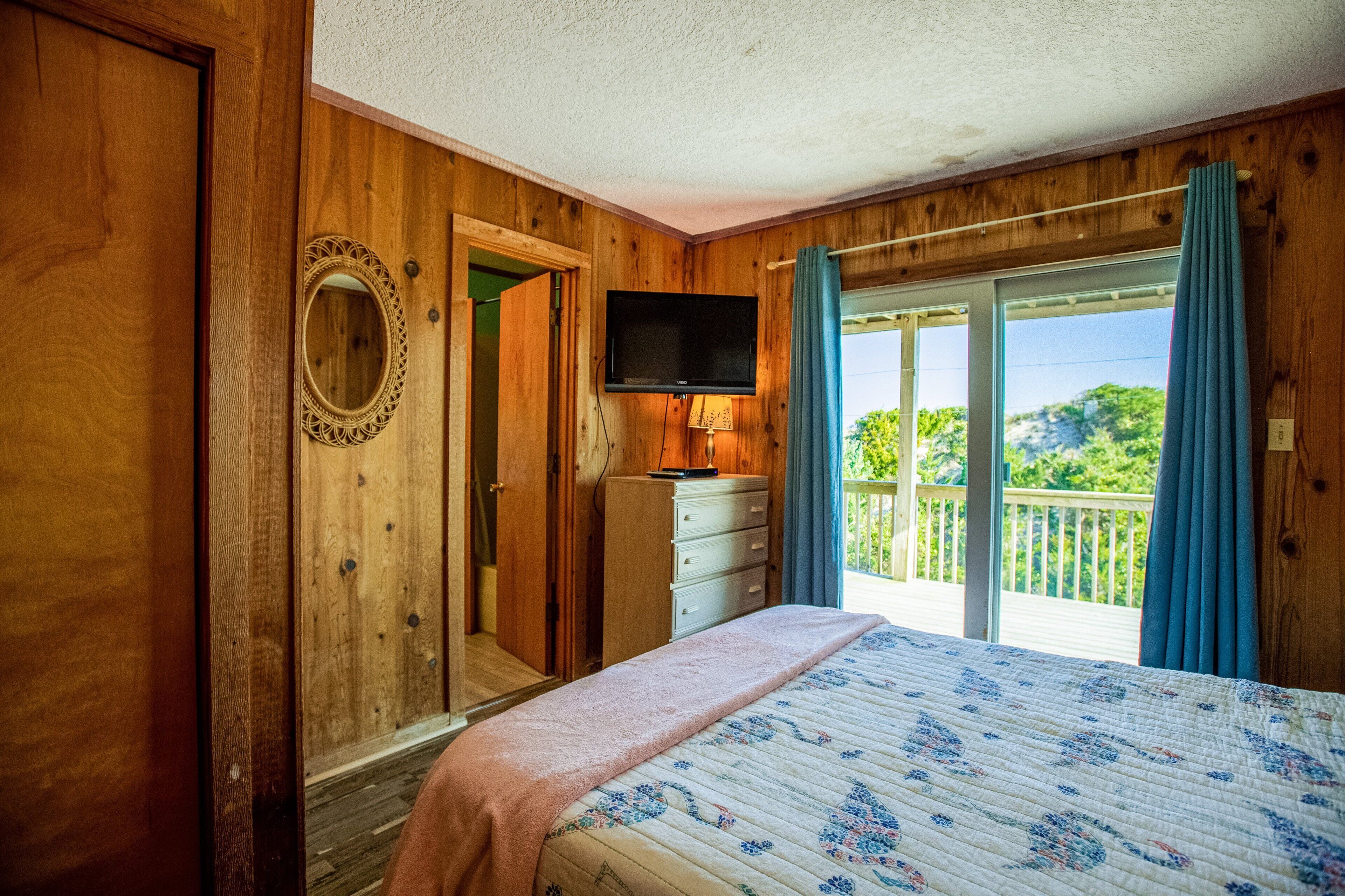Une chambre avec un lit, une commode, une télévision et un balcon offrant une vue.