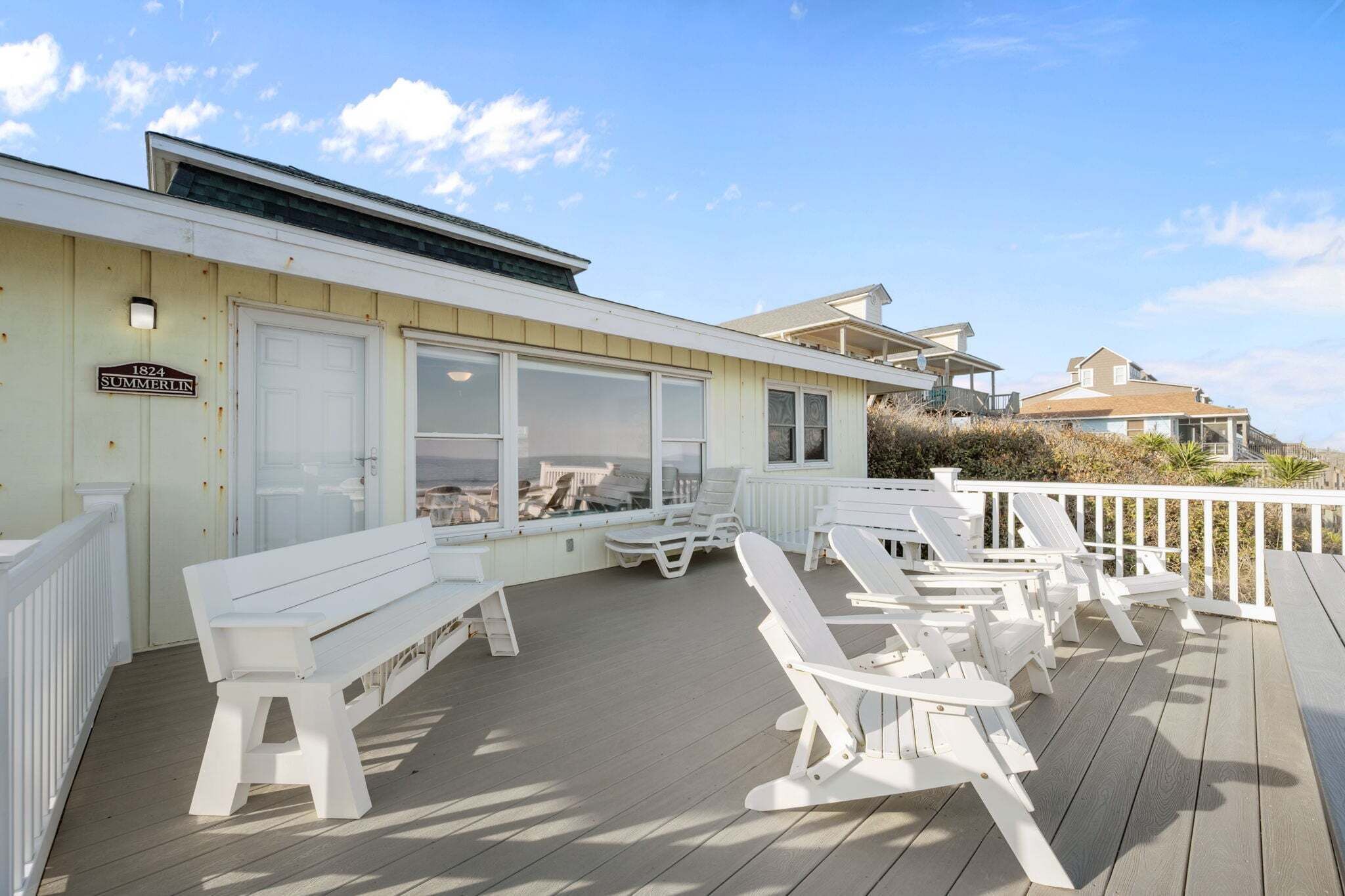 A deck with white chairs and a bench, a building with a sign reading '1824 SUMMERLIN,' and a view of the ocean.