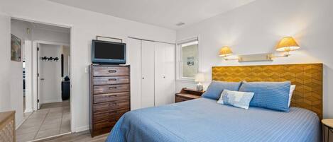 A bedroom with a bed, a TV, a dresser, a nightstand, and wall-mounted lamps.