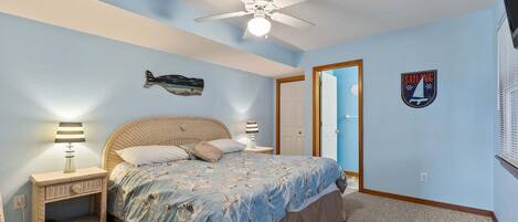 A bedroom with a bed, a ceiling fan, a wall-mounted fish decoration, a sailboat sign, and a door.