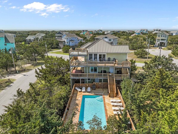 A two-story house with a pool, surrounded by trees and other houses.