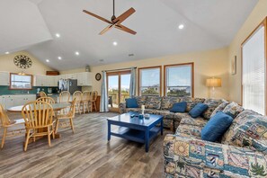A spacious living area with a dining table, chairs, a sofa, and a ceiling fan.