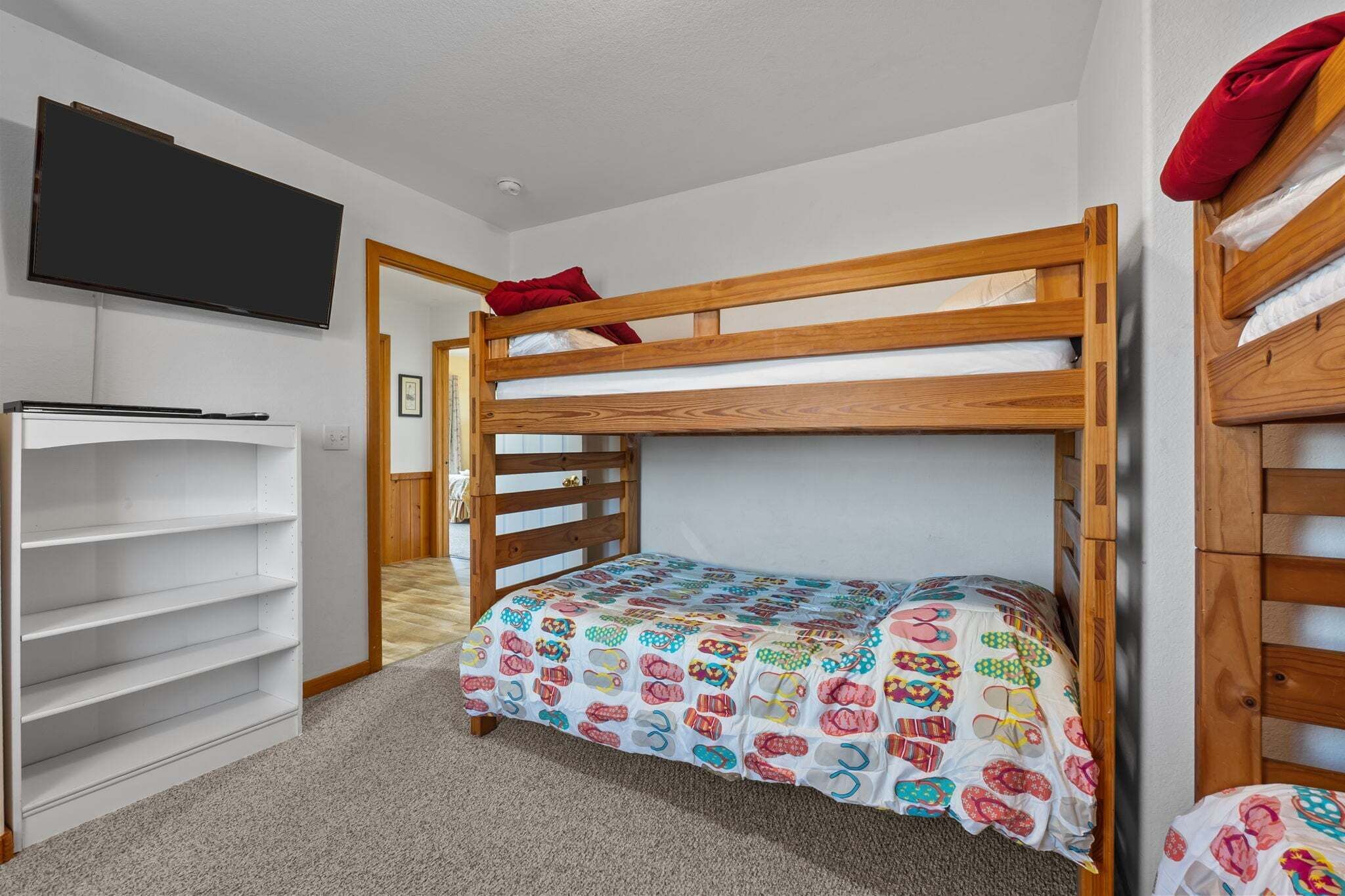 A bunk bed with a colorful bedspread, a white shelving unit, and a mounted television.