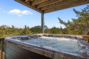 A hot tub with a wooden deck and a clear view of houses and trees in the background.