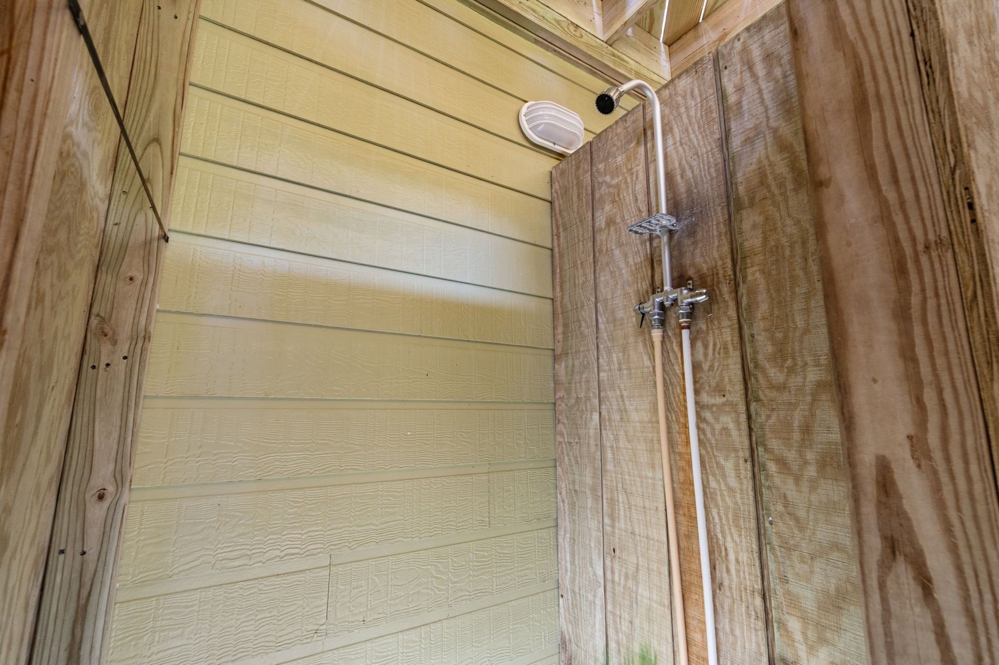 Une cabine de douche en bois équipée d’un pommeau de douche à main et d’un robinet fixé au mur.