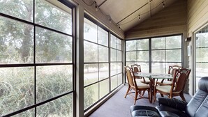 A sunroom with large windows, a dining table with chairs, and a leather sofa.