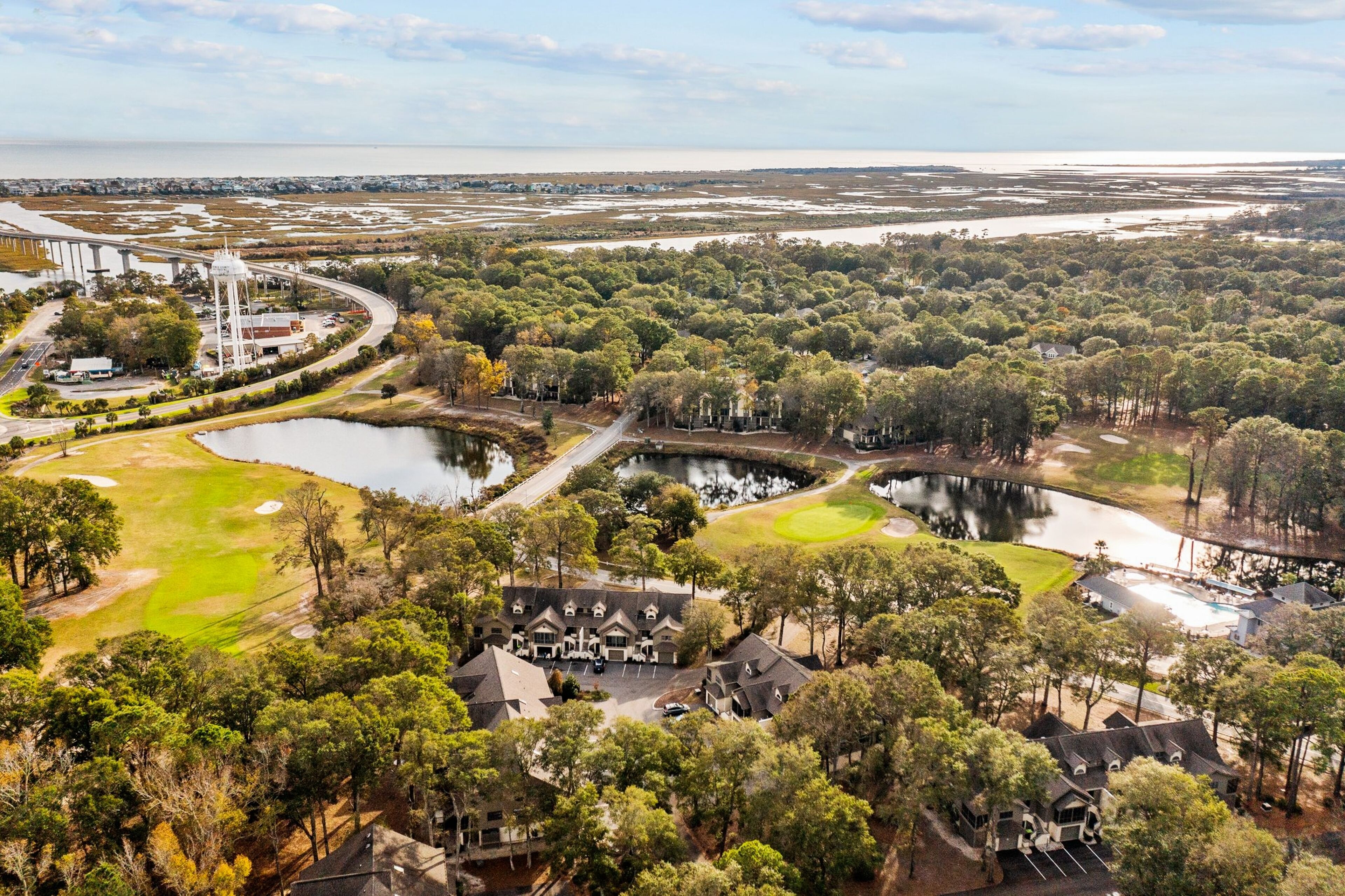 Un campo de golf con varios estanques, rodeado de árboles densos y algunos edificios.