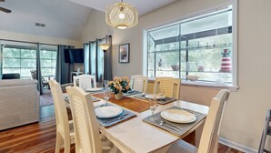 A dining area with a table set for six, surrounded by chairs, a hanging light fixture, and a window with blinds.
