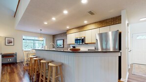A modern kitchen with a central island, wooden bar stools, and a large refrigerator.