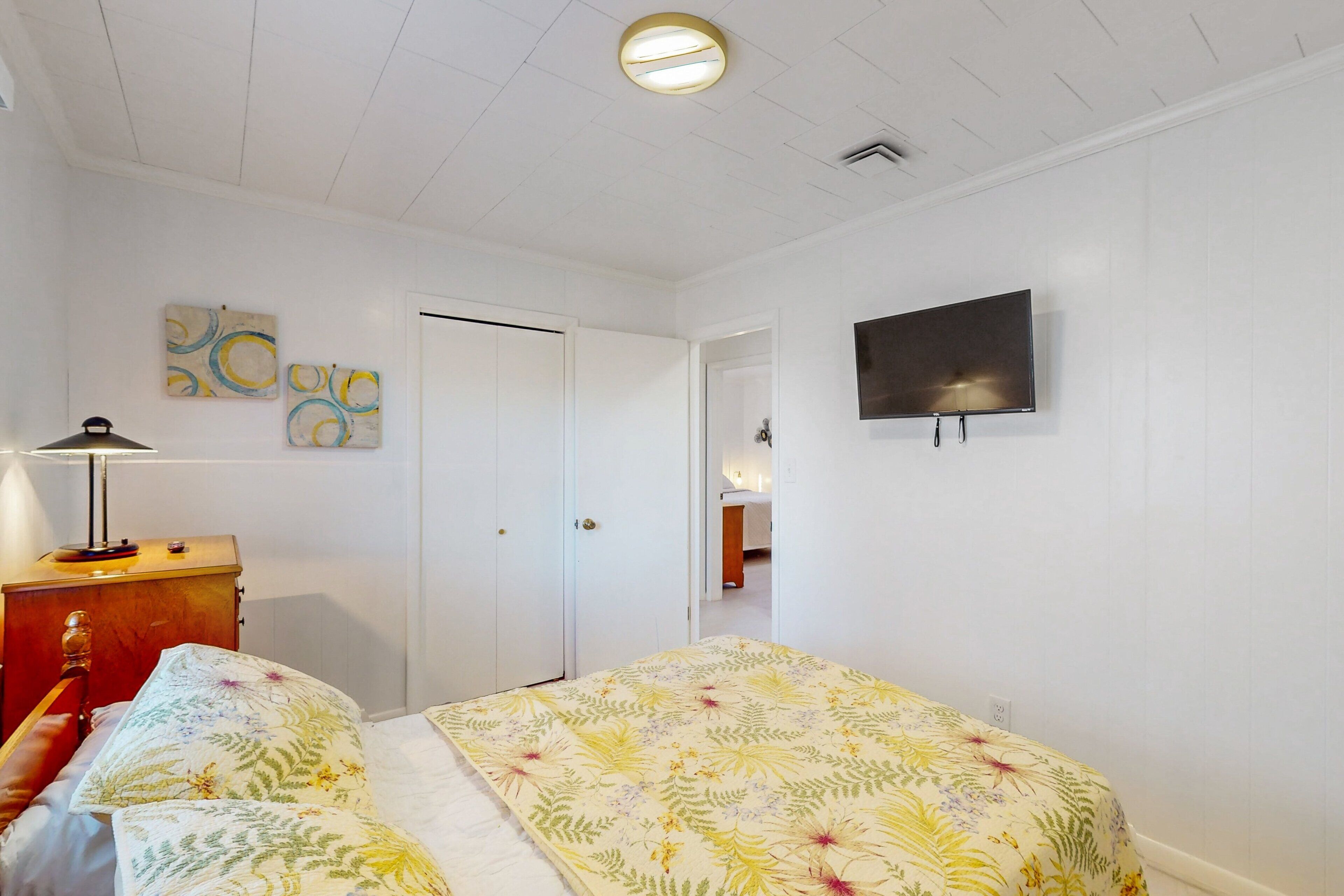 A bedroom with a bed, a TV mounted on the wall, and a door leading to another room.