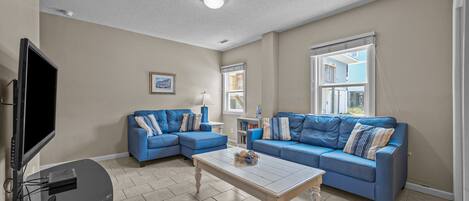 A living room with a sectional sofa, a coffee table, a flat-screen TV, and a window with blinds.