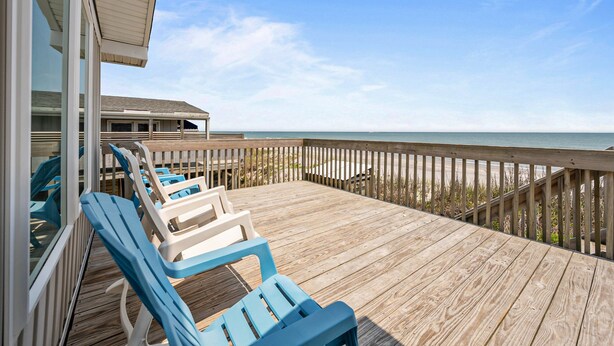 A wooden deck with blue and white lounge chairs, a wooden railing, and a view of the beach and ocean. - Oceanfront home with private beach access & outdoor shower - dog-friendly (Surf City)
