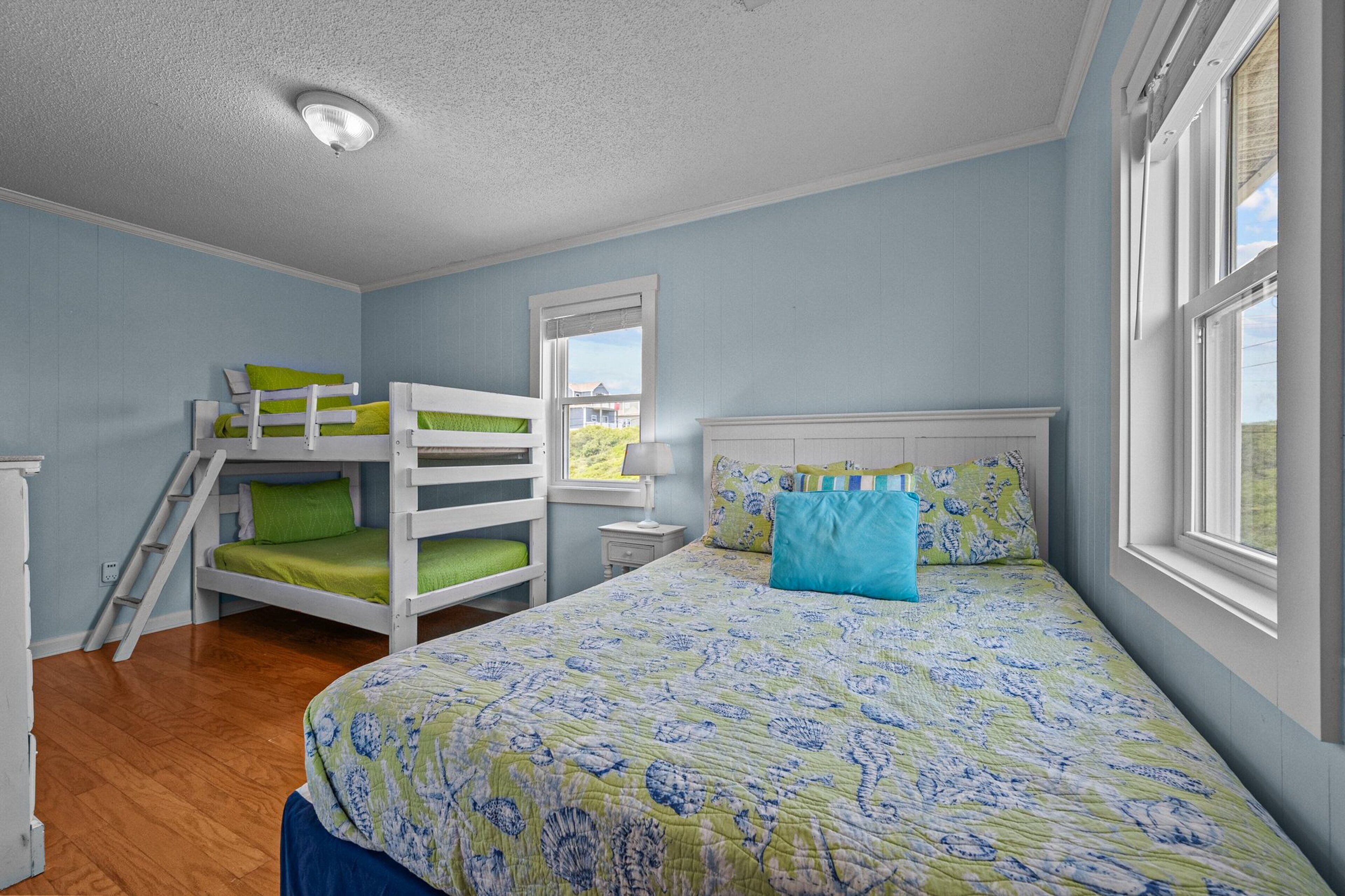 Une chambre avec un lit superposé, un grand lit avec une literie à motifs, une fenêtre donnant sur un paysage agréable et un luminaire au plafond.