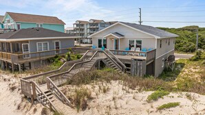 A beachfront property with a wooden staircase leading to a balcony, surrounded by sand dunes and vegetation. - Oceanfront home with private beach access & outdoor shower - dog-friendly (Surf City)