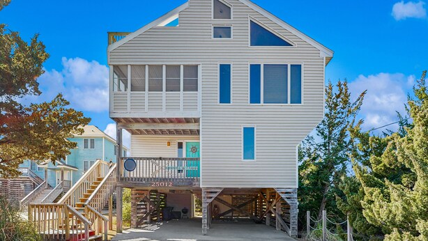 Une maison à deux étages avec un balcon, un garage dont la porte est visible et un escalier menant à l’étage supérieur.