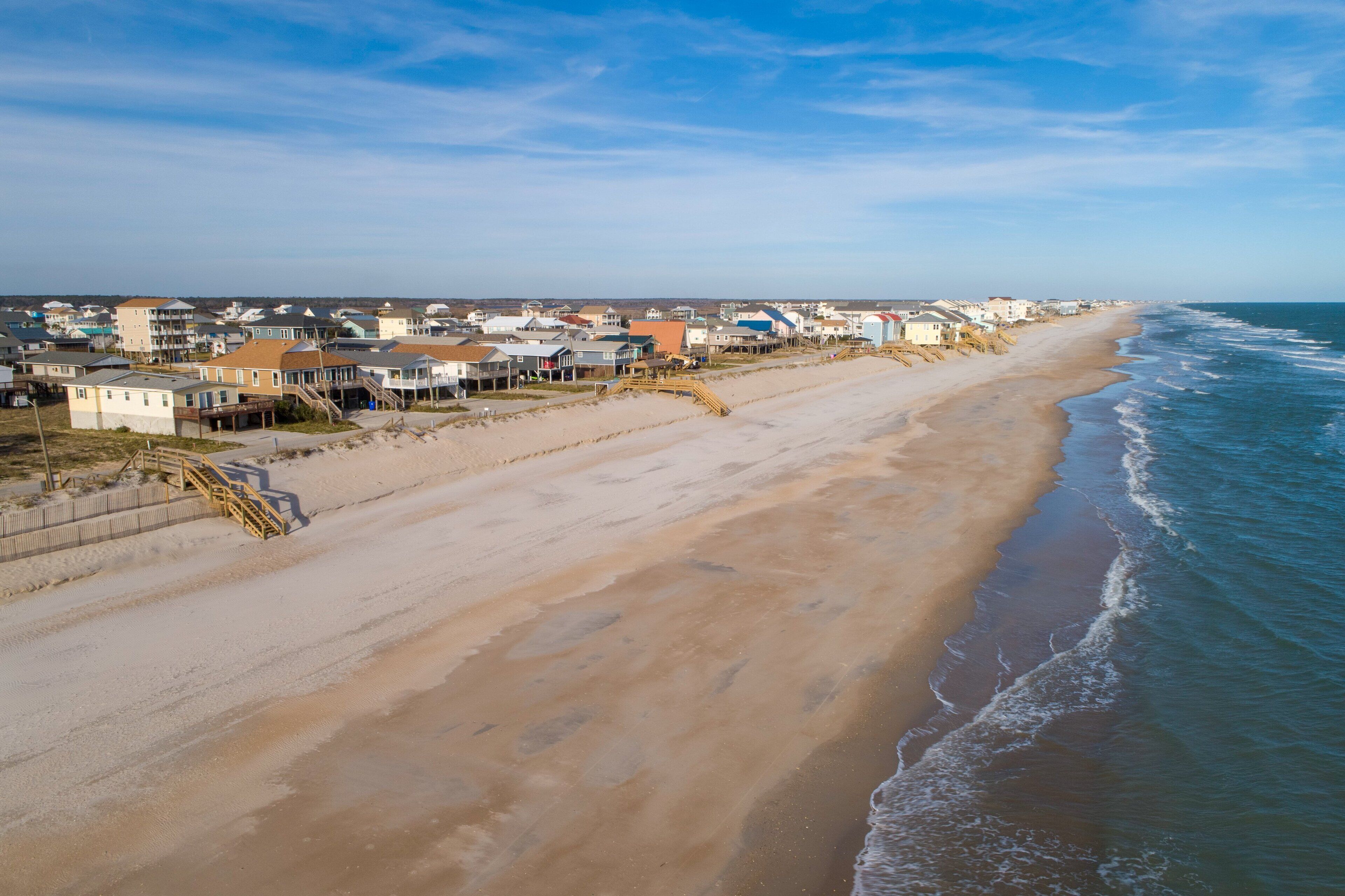 Un quartier résidentiel en bord de mer, avec des maisons le long de la plage, des promenades en bois et une vue dégagée sur l’océan.
