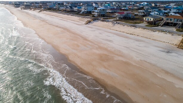 An aerial view of a beachside residential area with houses along the shoreline, a sandy beach, and waves approaching the shore. - Oceanview home with direct beach access just across the street (Surf City)