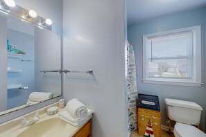 Een badkamer met een wastafel, spiegel, handdoekhouder en een raam met jaloezieën.