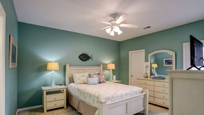 A bedroom with a bed, nightstands, a dresser, a ceiling fan, and a mirror. - Coral Hideaway: Balcony | Pool | Dog Friendly (Sunset Beach)
